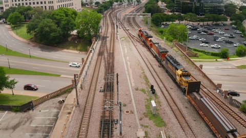 Three powerful diesel engines leading freight train around modern glass facade skyscrapers. Aerial drone view of slowly running train arriving to station. Dallas, Texas, US in 2021