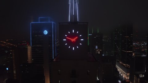 Colorful Neon illuminated spike and clock on top of Mercantile National Bank Building. Aerial drone night zooming out footage. Dallas, Texas, US in 2021