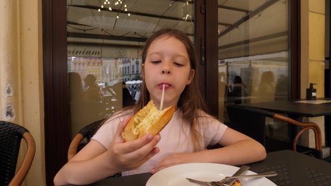 WROCLAW, POLAND - JUL 03, 2021: Child girl eating roasted bread with stretching cheese at street restaurant table