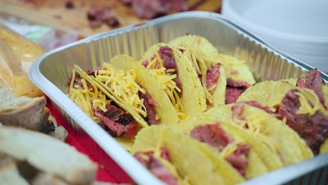 Preparation of bbq snacks on picnic party, man hand putting potato chips with raw meat pieces in aluminium foil pan and sprinkling with grated cheese for melting during roasting. Delicious recipes for