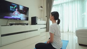 Asian beautiful girl follow sport training video to exercise in house. Young woman working out by watch online trainer and doing lockdown activity Yoga, Pilates exercise due to Coronavirus pandemic.