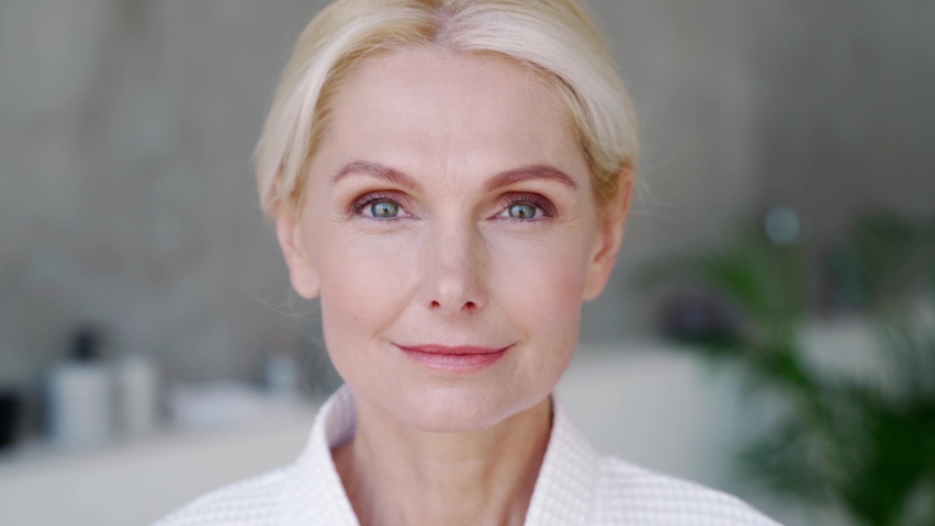 Closeup portrait of attractive middle aged blond woman wearing bathrobe with natural makeup looking at camera. Advertising of perfect antiage skin care products, hotel spa services concept. | Shutterstock HD Video #1075375556