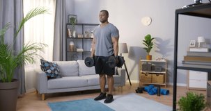 Full length view of the strong man lifting a dumbbell while having hard workout at home during the self isolation. Sport concept. Stock video