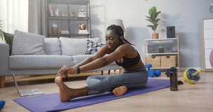 Full length view of the strong multiracial woman doing stretching and listening music while having hard workout at home during the self isolation. Sport concept. Stock video