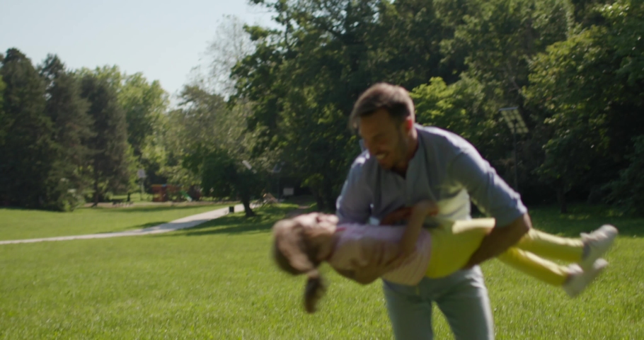 Father with cute little daughter having fun on the grass at the park