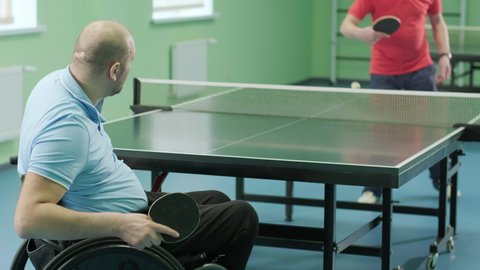 A man in a wheelchair plays ping pong. People with disabilities play table tennis. Rehabilitation of the disabled. Sport.