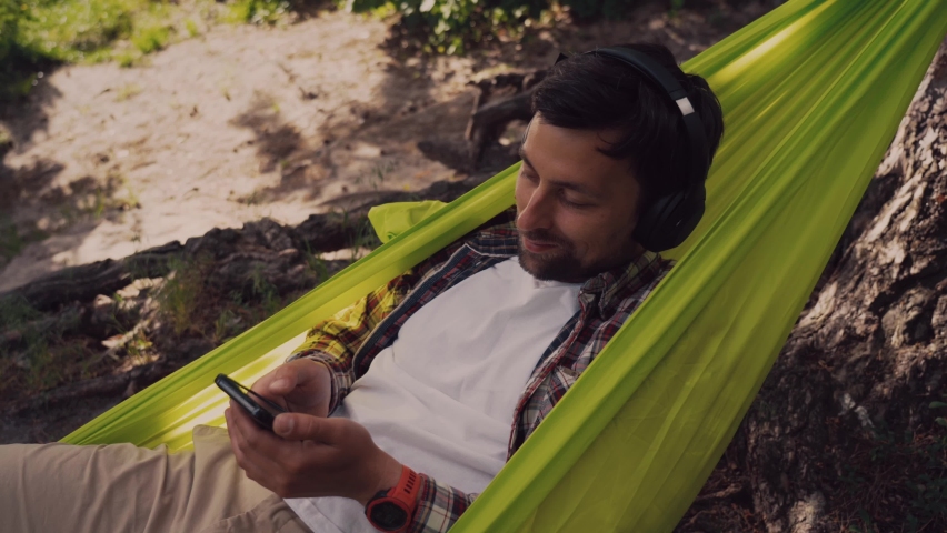 Young caucasian man resting in hammock, listening to music on headphones and using smartphone afterwards on bicycle in forest near the lake. Audio healing. Idyllic place. Travel, camping in nature - Powered by Shutterstock - Get 15% off with code: PIKWIZARD15