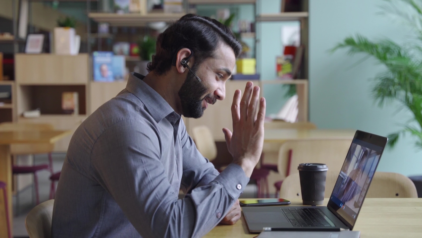 Indian business man wearing headset having virtual team meeting on video conference, call using laptop work from home office talking to diverse people group in remote teamwork online distance chat. | Shutterstock HD Video #1075387370