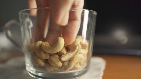 Picking roasted cashew nut from a cup