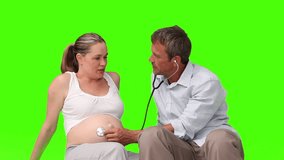 Man listening the belly of a pregnant woman thanks to a stethoscope against green screen