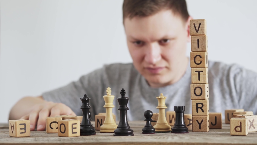 Happy man throws king. Victory over enemy. King in game of chess falls. In foreground is word victory made from wooden cubes. Throw opponent's chess king, the concept of triumph, success in business.
