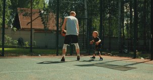 Sports basketball players trainer and little boy in action with ball outdoor on basketball court. Dribbling workout