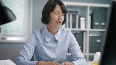 Depressed caucasian woman in blue shirt crying desperately while sitting at office table. Concept of people, feelings and burnout.