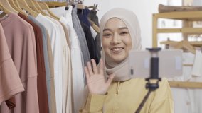 Young muslim woman selling her clothing. She using smartphone to live streaming with customer.