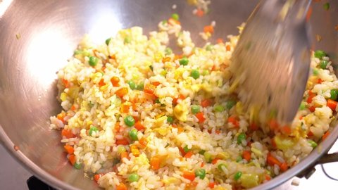Close-up of egg fried rice with carrots and green peas, using spatula to stir-fry the rice in the wok
