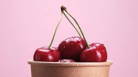 Ripe cherries in an eco-friendly cardboard cup rotate on a pink background video 4k.