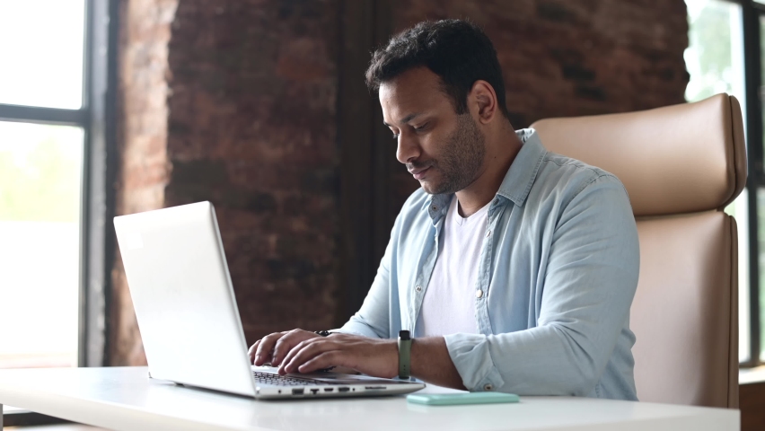 Desperate indian young male employee sitting at the desk and using laptop, closing it with irritation, businessman has financial problem, holding head with frustration face expression Royalty-Free Stock Footage #1075415012