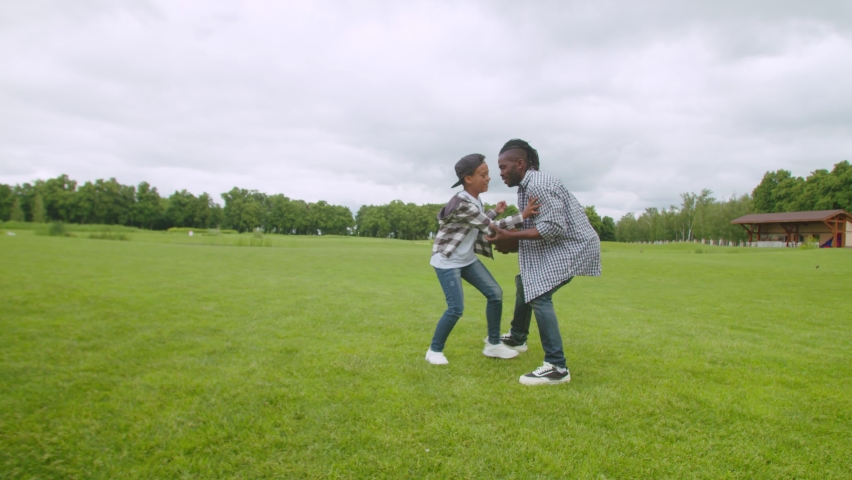 Excited playful lovely preadolescent african american boy tackling, wrestling carefree handsome father to the ground and fighting for ball while family having fun playing american football outdoor