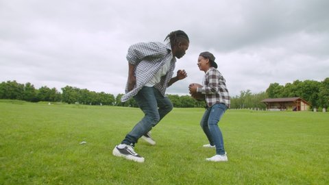 Side view of joyful cute school age black man carrying american football ball, passing defending handsome father and running to score goal while carefree family having fun playing football in nature.
