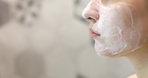 Woman is washing cleaning face with organic foamy soap cleanser, closeup view. Beauty procedure and skin care concept.