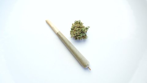 Marijuana joint next to a cannabis flower on a rotating white background