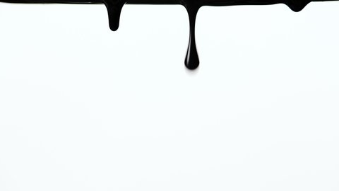 Black thick paint flows down on a white background close up. A drop forms and falls down. A large droplet of ink or paint dripping on white surface. Black isolated drops dripping in slow motion.