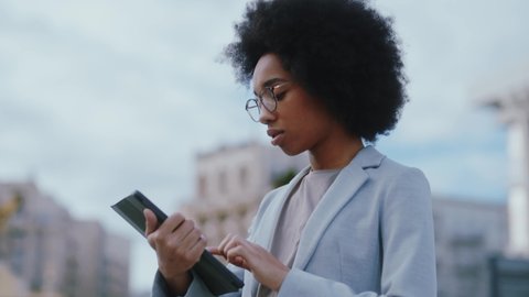 Black beautiful young woman engaged in business going to work using tablet computer reading financial news online. Afro hairstyle. Corporate people.