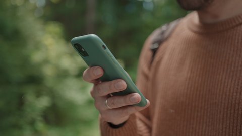 Close-up of a mobile phone in the hands of a male traveler walking through the forest. Social networks Navigator and messenger. Use your mobile phone for a walk in the woods