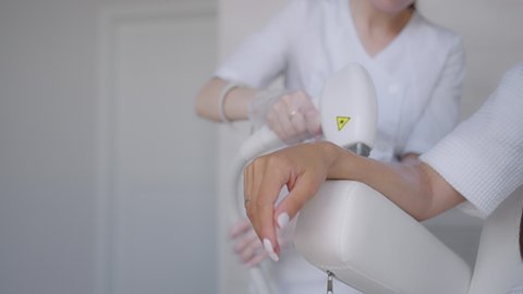 Procedure of removing hairs on hand. Laser hair removal on a diode laser, tracking moving camera. Woman cosmetologist applies laser hair removal gel on female hand. photoepilation, body care concept.