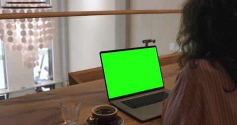 Young woman is working on a computer with a mock-up green screen. Digital nomad work remotely in restaurant. Software developer, Photographer, Digital Art Artist, NFT technology