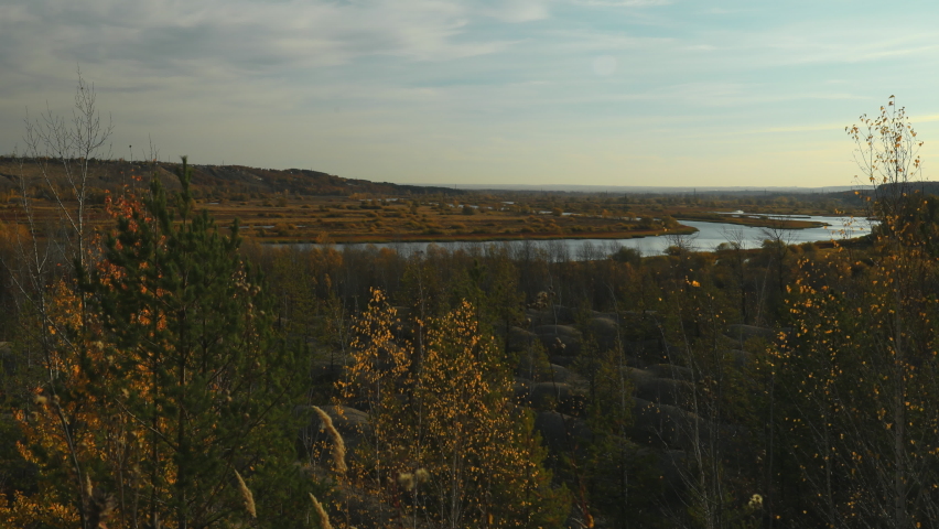 Morning landscape shot in time laps. Calm waters of a quiet flat river flow through a wide valley. Red autumn birch forest around. The low morning sun illuminates the landscape.