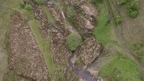 Drone footage looking down onto green countryside with trees and a flowing stream. Incredible view point of beautiful nature. 