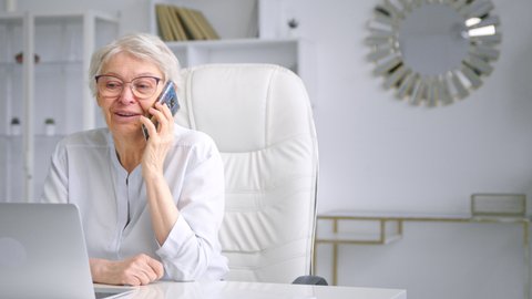 Smiling old woman corporate manager talks on blue smartphone
