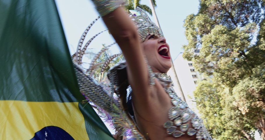 Beautiful Brazilian woman wearing colorful Carnival costume and Brazil flag during Carnaval street parade in city. 4K.