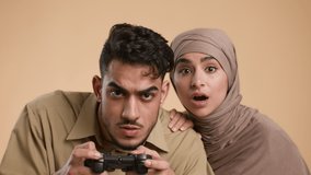 Muslim Millennial Couple Playing Video Game Together Posing Over Beige Studio Background, Looking At Camera. Modern Fun, Technology And Computer Gaming Concept.