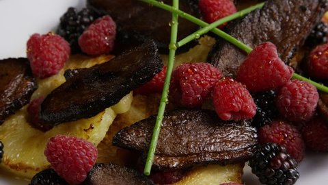 Rotating shot of a delicious dish with grilled pineapple, raspberries, and smoked duck bacon