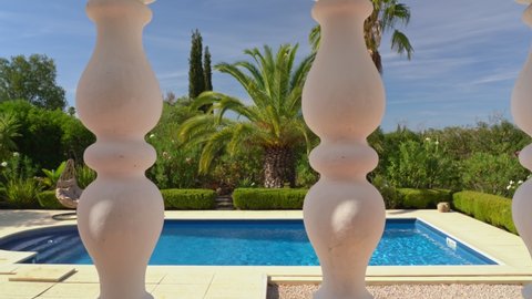 The movement of the video camera from left to right, to the side, stone columns of the terrace, the balcony of the villa, overlooking the beautiful pool. A garden with palm trees for tourists.