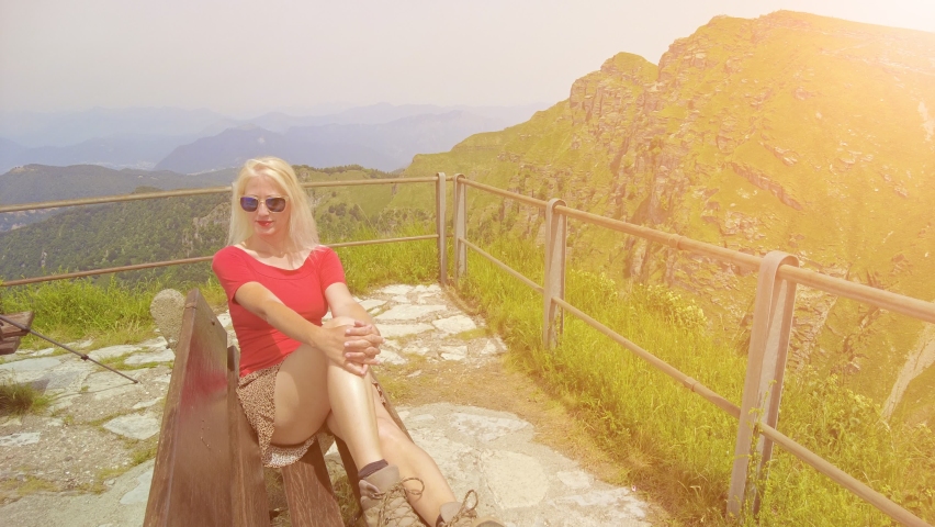 Tourist woman sitting at sunset on top view of Monte Generoso or Calvagione Swiss mount. Aerial skyline of Lugano lake of Ticino canton. Top of cog train station in Mendrisio district, Switzerland.