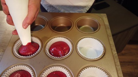 squeezing cupcake dough into cupcake holders in a baking tray
