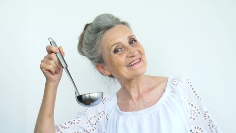 Emotional senior woman with silver hair is holding metal ladle or scoop on white background, happy retirement, mothers day concepts.