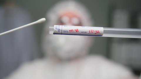 Close-up of PCR test in laboratory, doctor holding COVID-19 Coronavirus swab collection kit, wearing PPE protective uniform, test tube for taking OP NP patient specimen, PCR DNA testing protocol