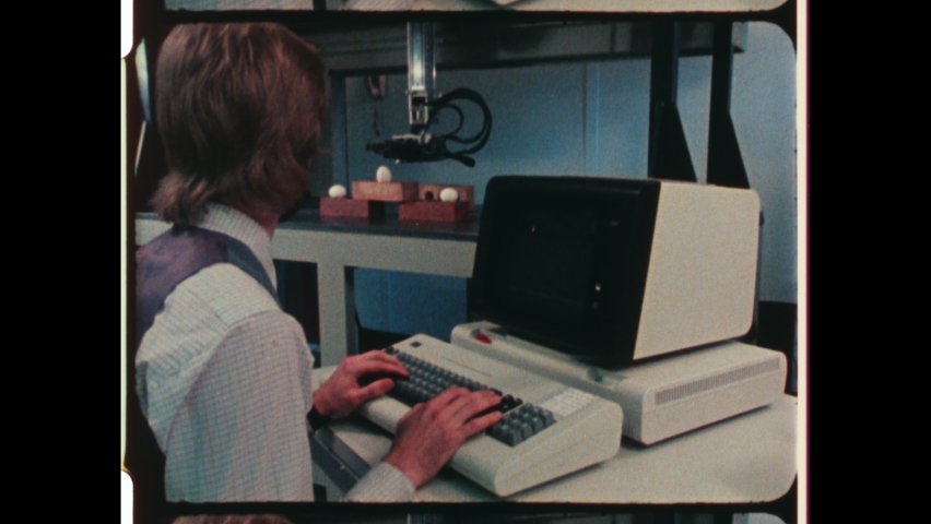 1980s Pittsburgh, PA. Man using IBM Computer programming or coding Industrial Robotic Arm. Green Text on early CRT Computer Screen. 4K Overscan of Vintage Archival 16mm Film Print
