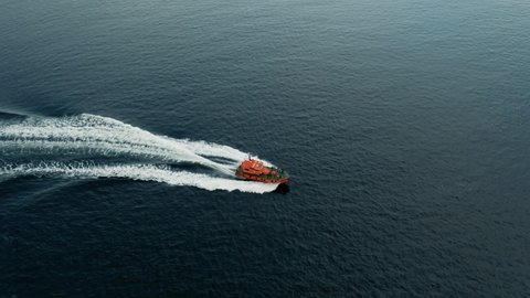 Aerial Drone Cinematic - chasing and circulating bright orange coast guard boat in the ocean right outside of the coast of Helsingborg Sweden and Helsingor Denmark in Oresund