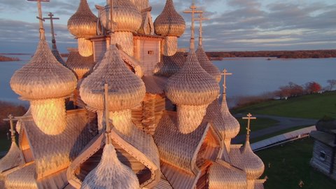 Aerial around Kizhi church wooden dome at orange scenic sunset Karelia travel landmark tample complex on island on lake. Russia traditional style no nais famous religious monument heritage. Sun bokeh