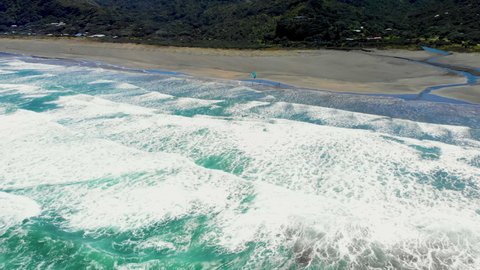 White Surfing Waves With Man Windsurfing At Piha Beach In New Zealand. - Aerial Shot