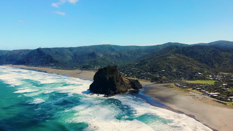 Lion Rock And Piha Black Sand Beach Under Bright Blue Sky In Auckland, New Zealand. aerial