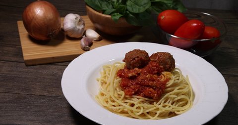 Stacking meatball on sauce cooked spaghetti white plate with ingredients roma tomato glass bowl basil onion garlic wooden board recipe on table marble wall 