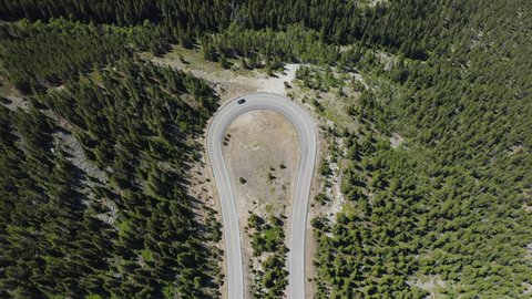 Aerial overhead view of the black car going slow up on curve high mountain asphalt road along green trees