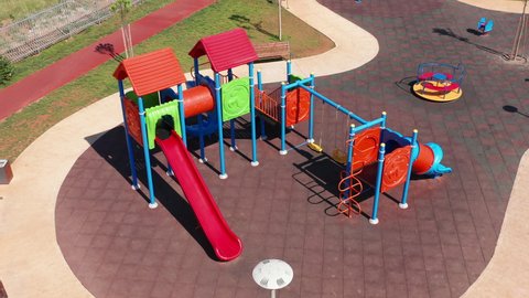 Empty playhouse and slide in a playground for kids. Deserted kindergarten park in residential neighborhood of a city during lockdown. Aerial view of colorful plastic equipment made for children play.