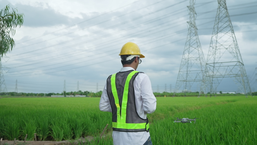 Electrical engineers in yellow safety helmets Drones are being used to inspect high-powered electric poles. located in a vast grassland Royalty-Free Stock Footage #1075481396